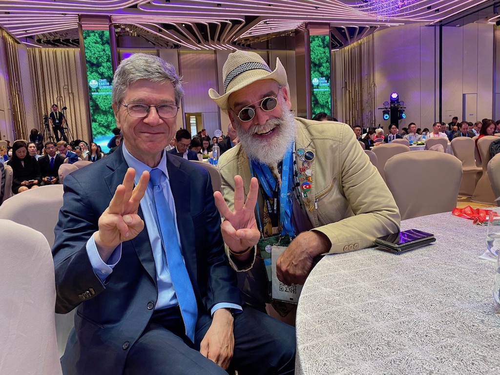 Professor Jeffrey Sachs and Philip McMaster (SustainaClaus) seated together, both raising three fingers