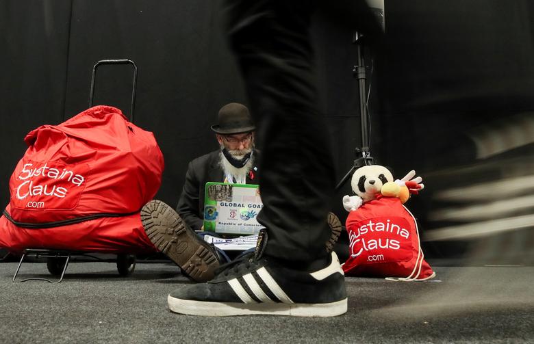 SustainaClaus seated with his red SustainaClaus bags at a UN climate conference as delegates walk past